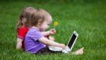 Two little children working together on the meadow with a laptop.