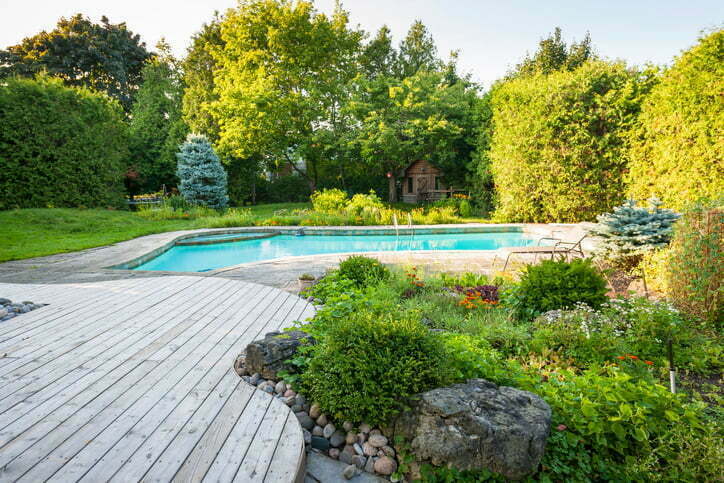 Backyard rock garden with outdoor inground residential swimming pool, curved wooden deck and stone patio