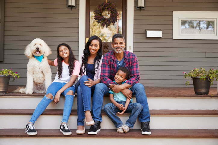 Family With Children And Pet Dog Sit On Steps Of Home