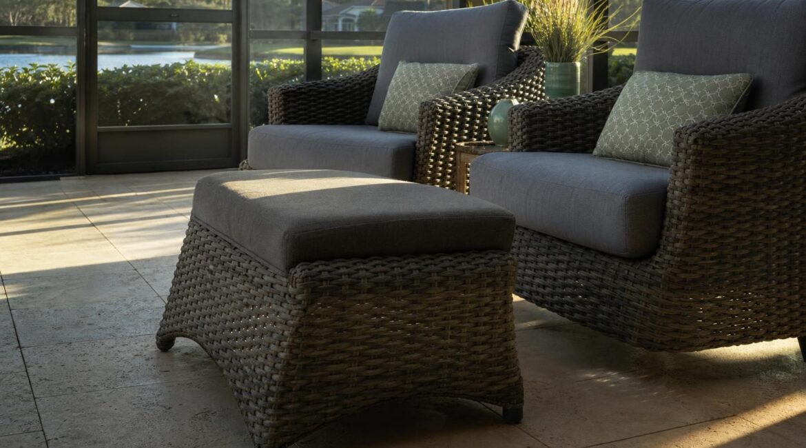 An outdoor wicker ottoman used as extra seating next to cushioned patio chairs on a Florida lanai