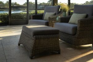 An outdoor wicker ottoman used as extra seating next to cushioned patio chairs on a Florida lanai
