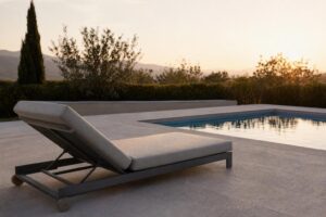 A cushioned aluminum chaise lounge positioned on a sunny pool deck beside a swimming pool