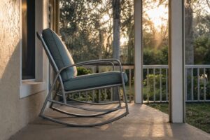 An aluminum-frame outdoor rocking chair with a cushioned seat on a Florida porch, side profile showing the curved base mechanism