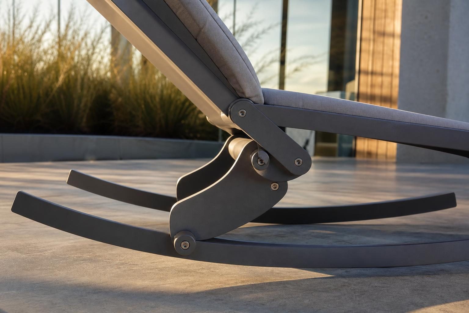 Close detail of a modern low-profile aluminum rocking chair's pivot base mechanism, side angle