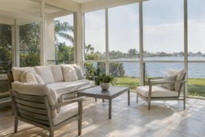 Cream-cushioned sofa and lounge chairs in a bright glass-enclosed sunroom with tall windows