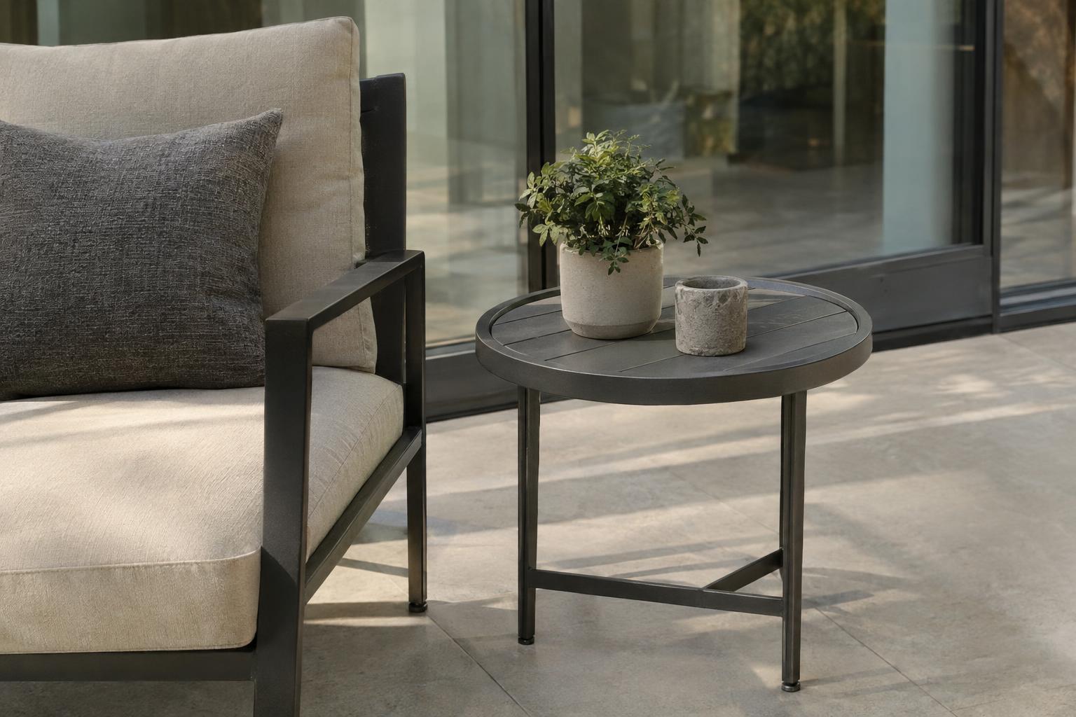 A small round side table beside a cushioned chair near a glass wall in a sunroom