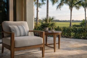 A teak side table beside a cushioned outdoor armchair on a covered patio